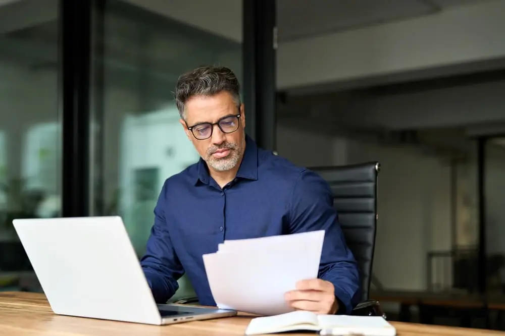 SKU-Level Risk Forecasting businessman with glasses reviewing reports on paper and on his laptop in his office